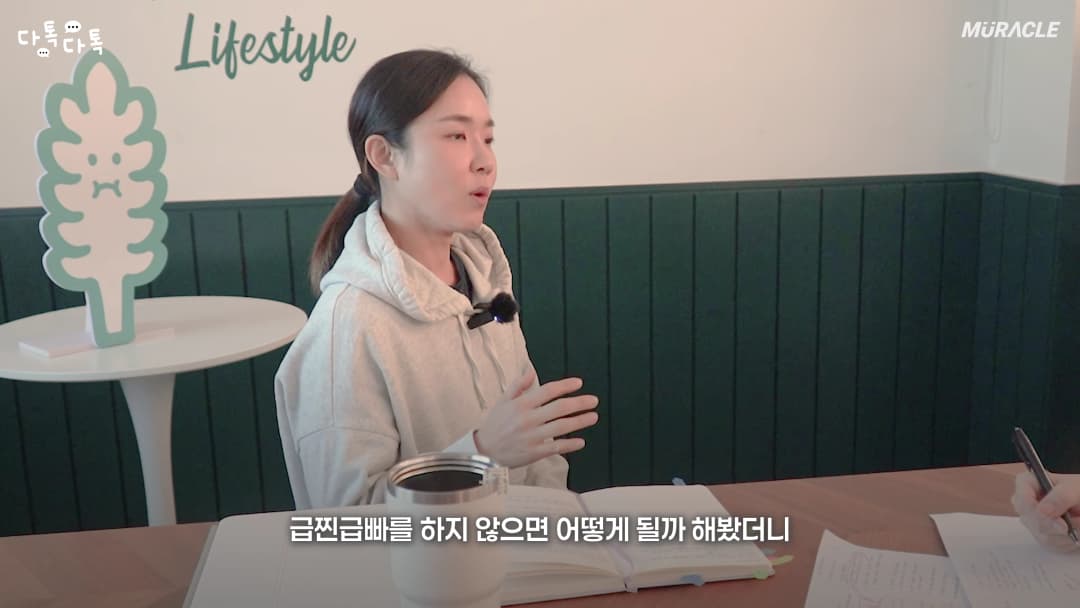 후드티를 입은 여성이 테이블에 앉아 대화하며 손짓으로 설명하는 모습