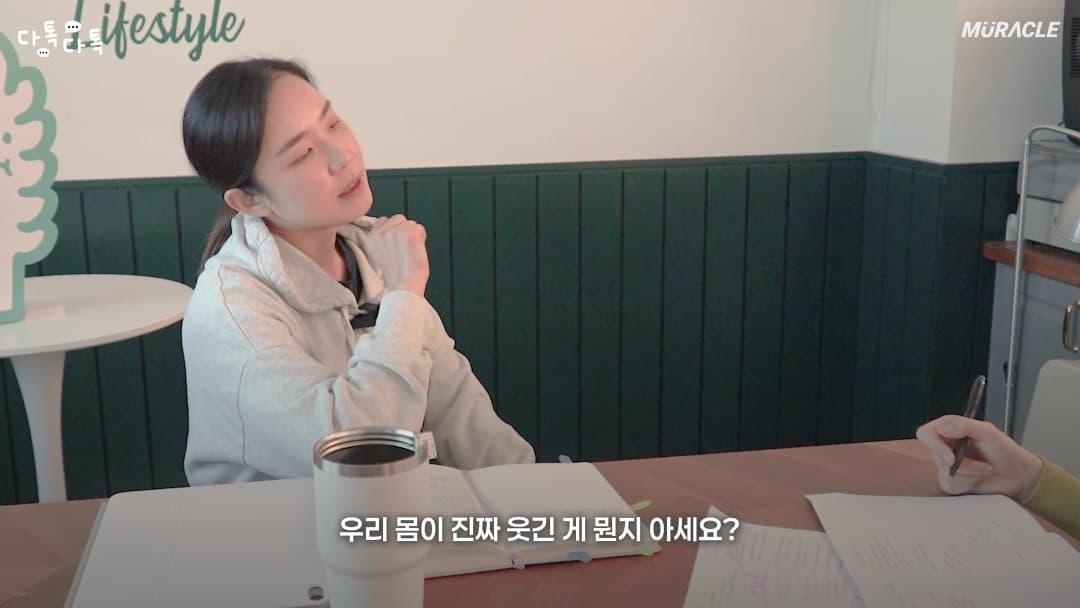 밝은 실내에서 한 여성이 테이블에 앉아 대화하는 모습이 담긴 영상 캡처 화면