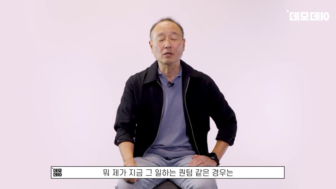 밝은 배경 앞에서 검은 재킷을 입은 중년 남성이 앉아 인터뷰를 진행하고 있다.