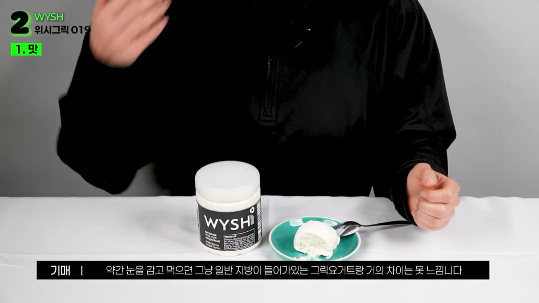 검은 옷을 입은 사람이 테이블 위에 놓인 요거트 제품과 접시에 담긴 요거트를 소개하고 있다.