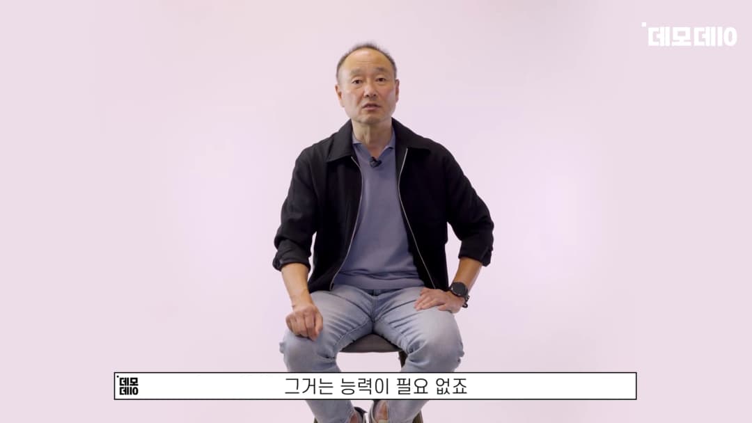 밝은 배경의 스튜디오 의자에 앉아 정면을 응시하며 이야기하는 중년 남성