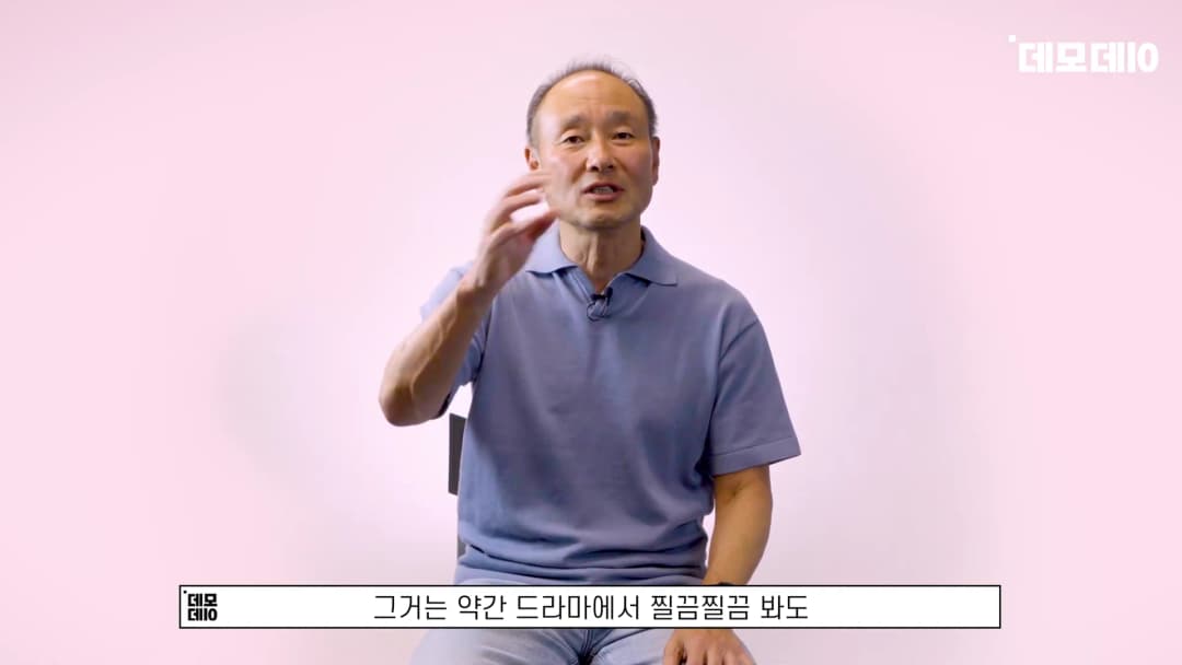 분홍색 배경 앞에서 파란색 폴로 셔츠를 입은 중년 남성이 손짓하며 이야기하는 모습
