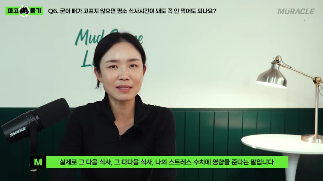 검은색 상의를 입은 여성이 스튜디오에서 마이크를 앞에 두고 이야기를 나누고 있다.