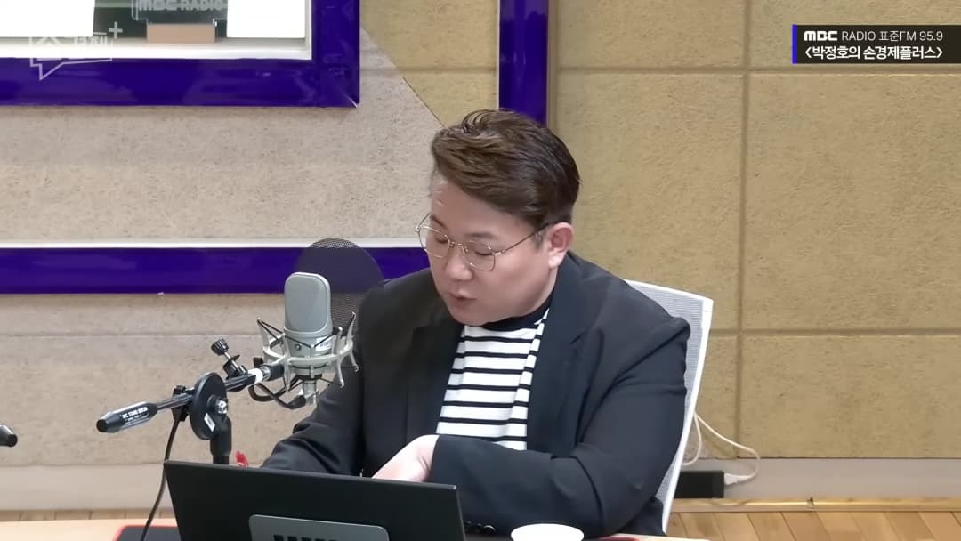 라디오 스튜디오에서 검은색 재킷을 입고 마이크 앞에 앉아 노트북을 보고 있는 남성
