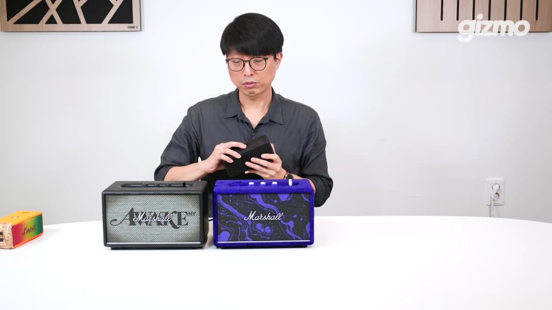 안경을 쓴 남성이 테이블 위에 놓인 두 대의 마샬 스피커를 비교하며 살펴보고 있다.