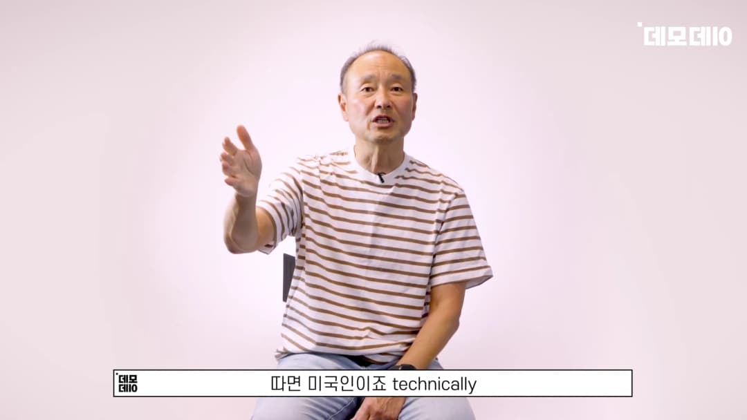 흰색 배경 앞에서 줄무늬 티셔츠를 입은 중년 남성이 손을 들어 제스처를 하며 이야기하고 있다.