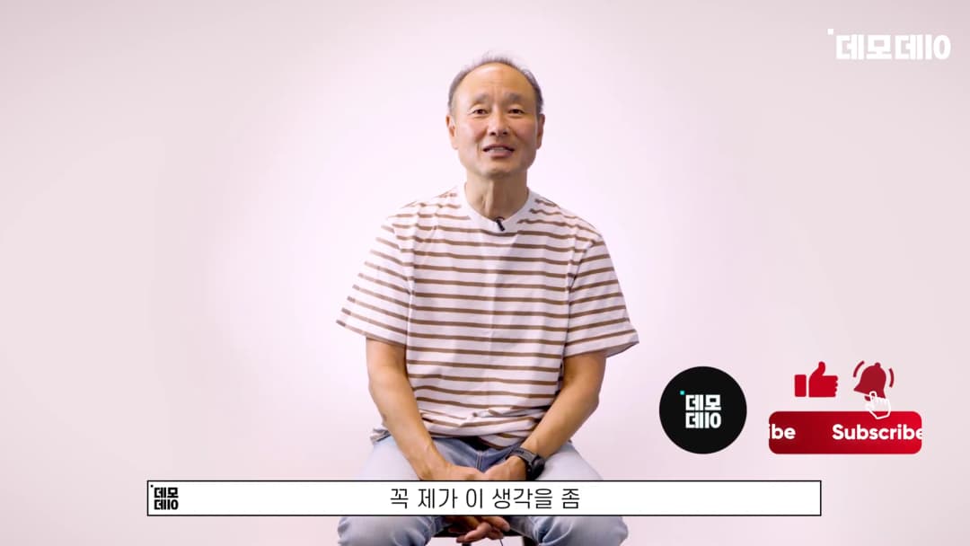 줄무늬 티셔츠를 입은 중년 남성이 밝은 배경 앞에서 인터뷰하고 있다.