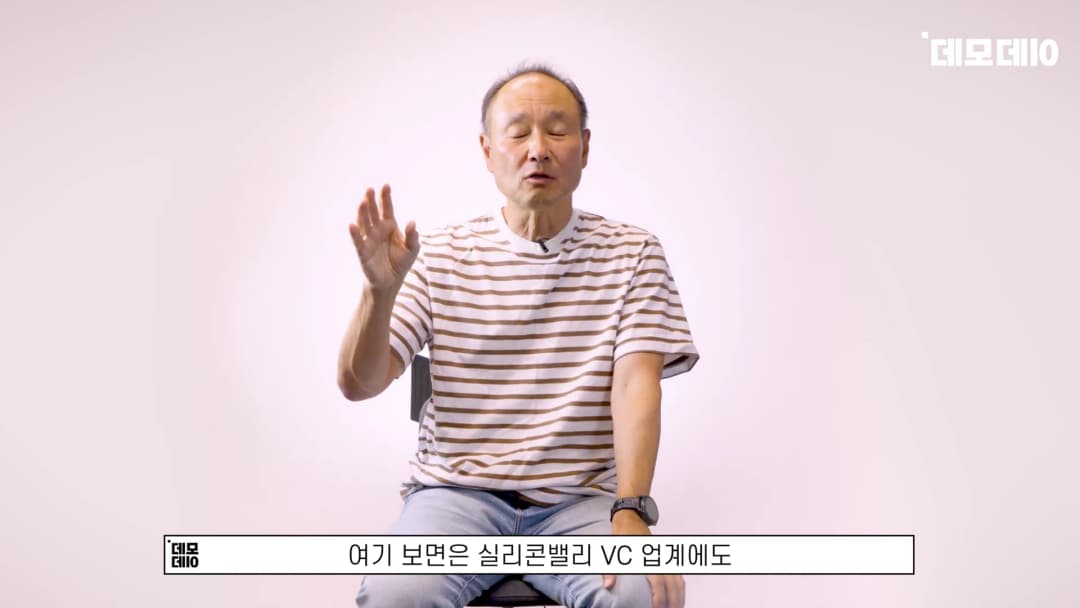 줄무늬 티셔츠를 입은 중년 남성이 밝은 배경 앞에서 손을 들어 대화하고 있는 모습