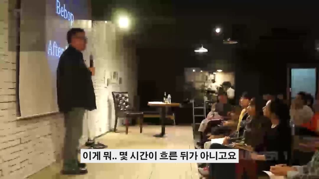 강연자가 스크린 앞에 서서 청중을 향해 마이크를 잡고 이야기하는 강연장 모습