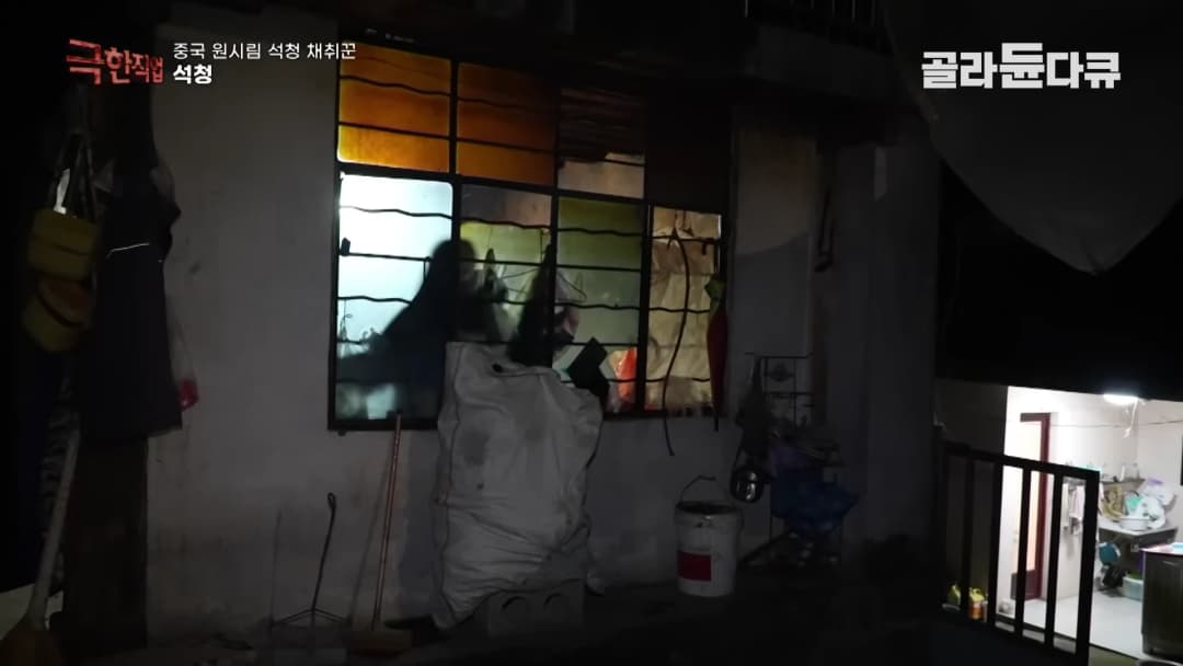 어두운 밤, 창문 안쪽에서 불빛이 새어 나오는 시골집 외관과 그 앞의 살림살이들